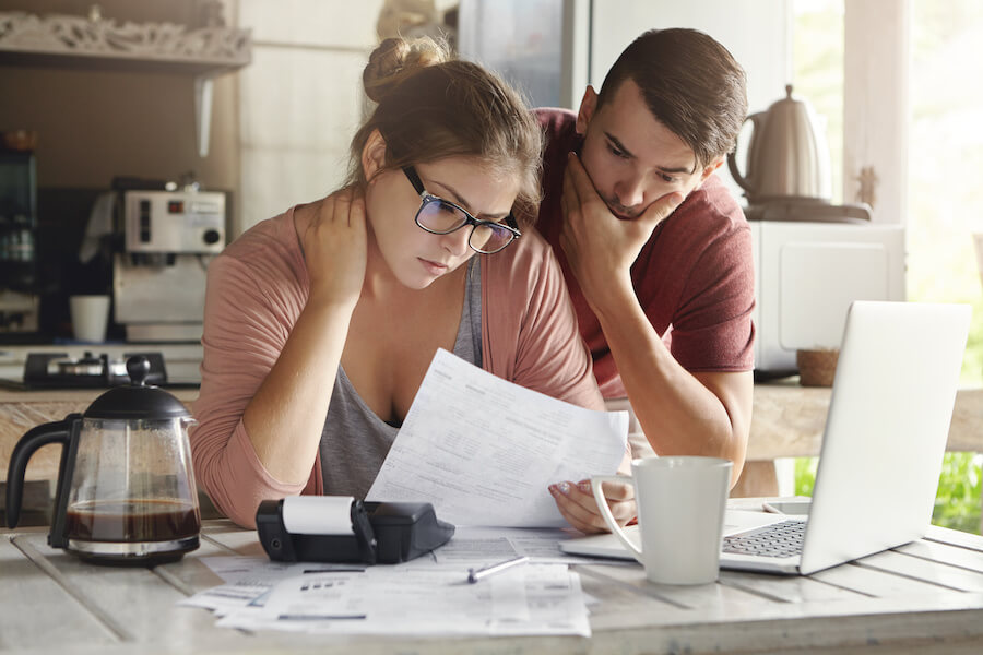 young couple in kitchen looking a a bill with a laptop